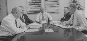 A group of lawyers discussing a legal case around a conference table, with documents and a binder in front of them.