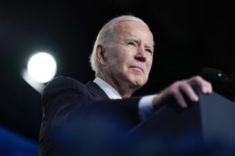 Close-up of a person speaking at a podium with a spotlight in the background.