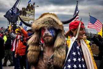 A man wearing a Viking-style headdress and face paint stands among a crowd, holding a spear with an American flag attached, during the Capitol riot on January 6.