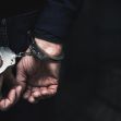 Hands secured in handcuffs behind a person's back, with a dark background. Hands secured in handcuffs behind a person's back, with a dark background.
