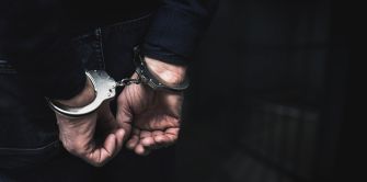 Hands secured in handcuffs behind a person's back, with a dark background.