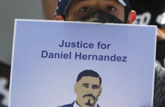 A person holding a sign that reads "Justice for Daniel Hernandez," featuring an illustration of a man in a suit.