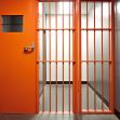 Empty solitary confinement cell with an orange door and barred entrance. Empty solitary confinement cell with an orange door and barred entrance.