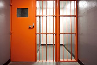 Empty solitary confinement cell with an orange door and barred entrance.