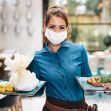 A waitress wearing a mask holds two plates of food in a restaurant setting. A waitress wearing a mask holds two plates of food in a restaurant setting.