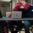 A family sitting together, expressing their emotions and support for one another at a table with a laptop in a home setting. A family sitting together, expressing their emotions and support for one another at a table with a laptop in a home setting.