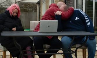 A family sitting together, expressing their emotions and support for one another at a table with a laptop in a home setting.