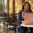 Woman sitting at an outdoor café with a laptop, appearing to work or engage in a creative task. Woman sitting at an outdoor café with a laptop, appearing to work or engage in a creative task.