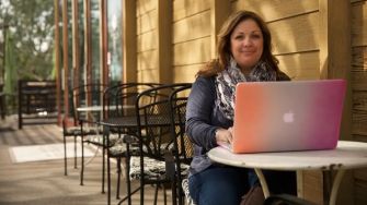 Woman sitting at an outdoor café with a laptop, appearing to work or engage in a creative task.
