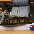A close-up of a book titled "Financial Crimes" with handcuffs placed on top, surrounded by papers in an office setting. A close-up of a book titled "Financial Crimes" with handcuffs placed on top, surrounded by papers in an office setting.