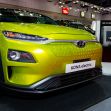 A bright green Hyundai Kona Electric vehicle displayed at an auto show alongside a charging station. A bright green Hyundai Kona Electric vehicle displayed at an auto show alongside a charging station.