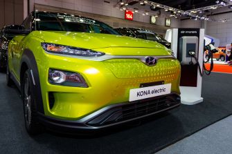 A bright green Hyundai Kona Electric vehicle displayed at an auto show alongside a charging station.