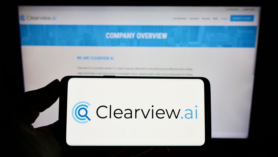 Clearview AI facial recognition software logo on the glowing screen and blurred faces from social media on the background.