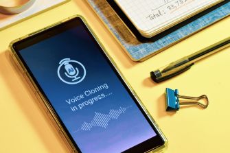 A smartphone displaying a message about voice cloning in progress, surrounded by office supplies.