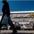 A person walking past a Walmart store, carrying a shopping bag, with the store's sign prominently displayed. A person walking past a Walmart store, carrying a shopping bag, with the store's sign prominently displayed.