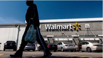 A person walking past a Walmart store, carrying a shopping bag, with the store's sign prominently displayed.