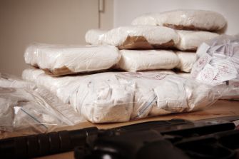 Bundles of packaged narcotics stacked on a table next to a firearm.