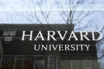 Harvard University sign displayed on a building window, with tree branches reflected in the glass.