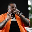 Sean Kingston performing on stage, wearing an orange shirt and holding a microphone. Sean Kingston performing on stage, wearing an orange shirt and holding a microphone.