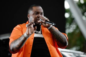 Sean Kingston performing on stage, wearing an orange shirt and holding a microphone.