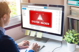 A person sitting at a computer with a warning message on the screen indicating that the system has been hacked.