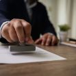 A person using a stamp to seal documents on a wooden desk. A person using a stamp to seal documents on a wooden desk.