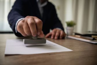 A person using a stamp to seal documents on a wooden desk.