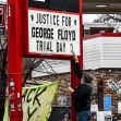 A person adjusts a sign that reads "Justice for George Floyd Trial Day 3" outside a building covered in graffiti. A person adjusts a sign that reads "Justice for George Floyd Trial Day 3" outside a building covered in graffiti.