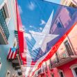 A large Puerto Rican flag hangs between colorful buildings in a street, symbolizing the island's ongoing discussions about statehood and political status. A large Puerto Rican flag hangs between colorful buildings in a street, symbolizing the island's ongoing discussions about statehood and political status.