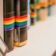 A row of books with rainbow-colored spine decorations, symbolizing LGBTQ+ themes. A row of books with rainbow-colored spine decorations, symbolizing LGBTQ+ themes.
