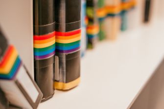 A row of books with rainbow-colored spine decorations, symbolizing LGBTQ+ themes.