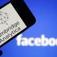 A smartphone displaying the Cambridge Analytica logo in front of the Facebook logo. A smartphone displaying the Cambridge Analytica logo in front of the Facebook logo.