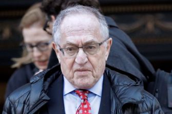 Alan Dershowitz walking outdoors, appearing serious and contemplative.