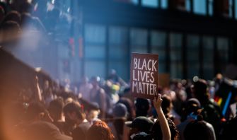 A protestor holds a sign that reads "BLACK LIVES MATTER" in a large crowd at a demonstration.