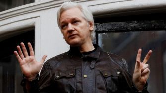 Julian Assange gesturing with peace signs outside a building.