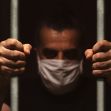 A man wearing a mask grips prison bars, highlighting the struggles of inmates during the COVID-19 pandemic. A man wearing a mask grips prison bars, highlighting the struggles of inmates during the COVID-19 pandemic.