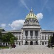 The Pennsylvania State Capitol building, an architectural landmark with a golden-domed roof, surrounded by trees and blue skies. The Pennsylvania State Capitol building, an architectural landmark with a golden-domed roof, surrounded by trees and blue skies.