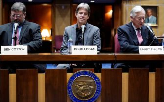 Panel of three men speaking at a table with microphones, including one identified as Doug Logan, during a legislative session regarding election audits.