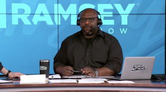Chris Hogan seated at a desk with a laptop and a coffee cup, hosting a segment of The Dave Ramsey Show.