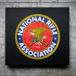 An emblem of the National Rifle Association (NRA) displayed on a wall. An emblem of the National Rifle Association (NRA) displayed on a wall.