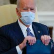 A seated President Biden wearing a mask, holding a binder, during a meeting. A seated President Biden wearing a mask, holding a binder, during a meeting.