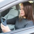 A woman sitting in a car is looking at her smartphone while driving. A woman sitting in a car is looking at her smartphone while driving.