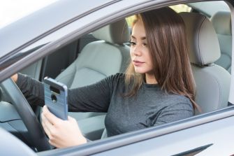 A woman sitting in a car is looking at her smartphone while driving.