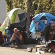 Two individuals near makeshift tents and belongings, illustrating the homelessness crisis in Los Angeles. Two individuals near makeshift tents and belongings, illustrating the homelessness crisis in Los Angeles.