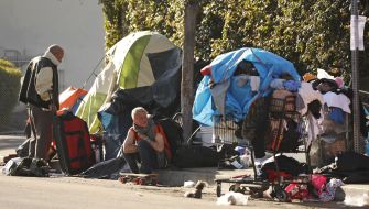 Two individuals near makeshift tents and belongings, illustrating the homelessness crisis in Los Angeles.