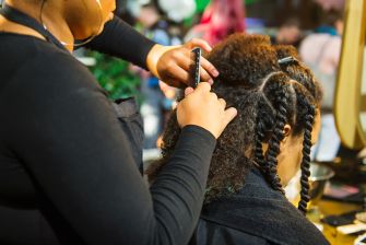 A person receiving hairstyling in a salon, focusing on natural and braided hairstyles.