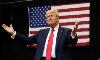 Donald Trump speaks at a campaign rally with an American flag in the background.