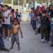 A crowd of people, including children, waiting in line in an outdoor setting. A crowd of people, including children, waiting in line in an outdoor setting.