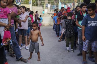 A crowd of people, including children, waiting in line in an outdoor setting.