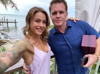 Christmas Abbott and Memphis Garrett posing for a selfie by the water, with palm trees and a pier in the background.
